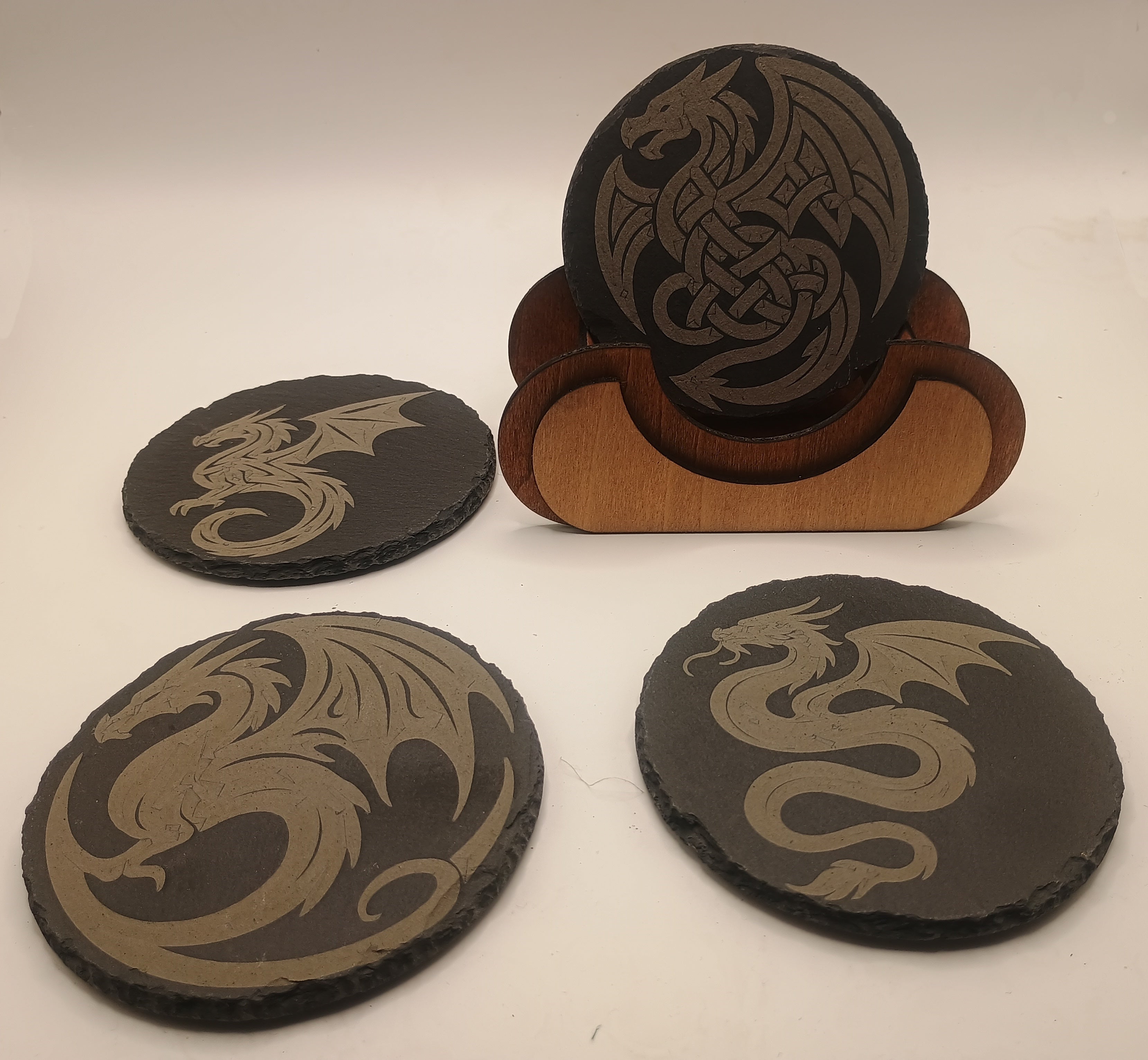 Four dragon-themed coasters with a wooden stand on a white background