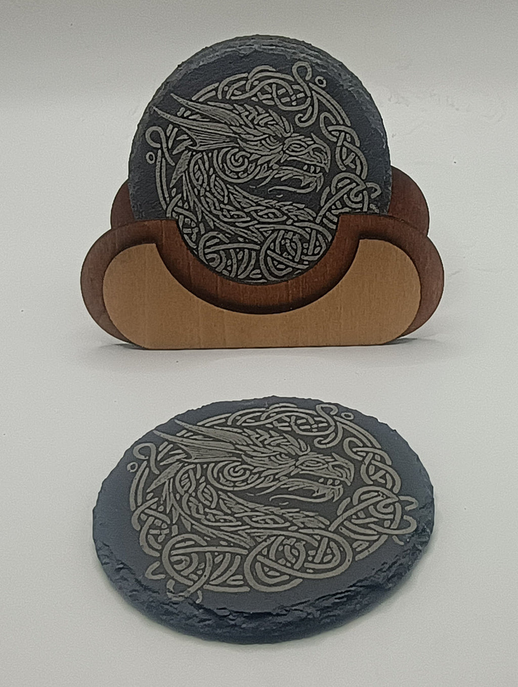 Two gray coasters with Celtic dragon design on a white surface
