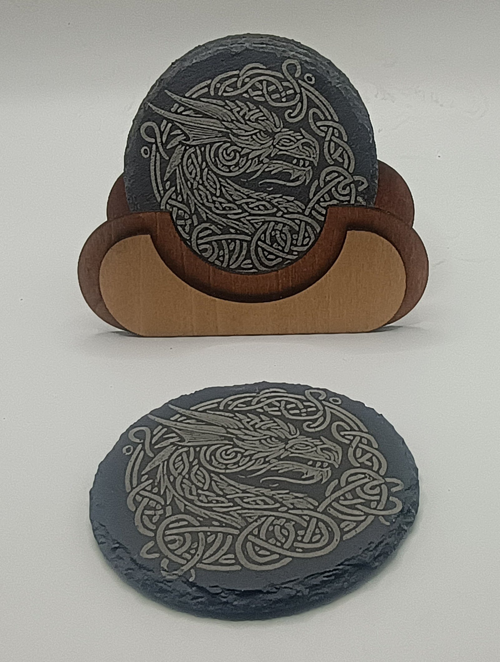 Two gray coasters with Celtic dragon design on a white surface