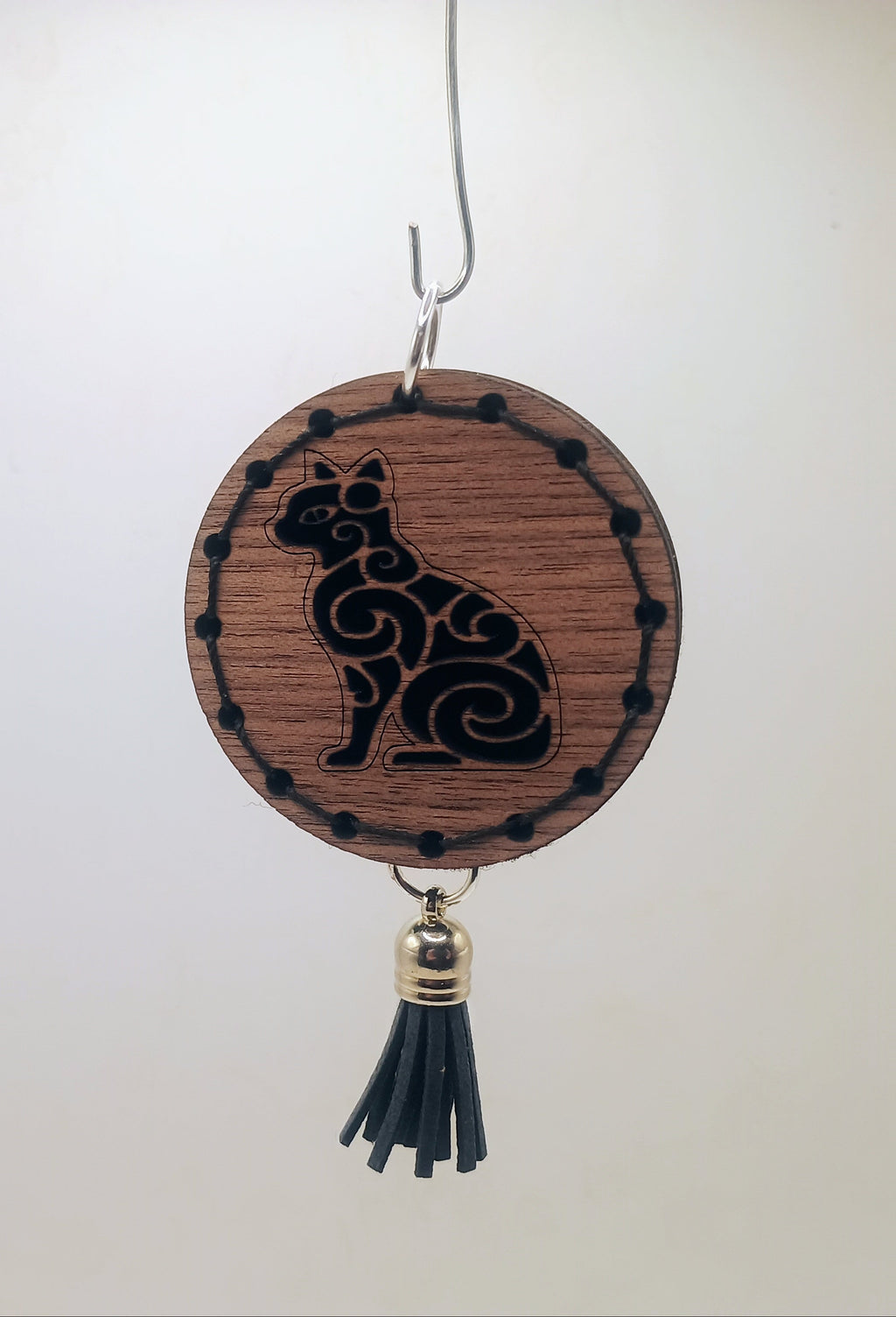Wooden ornament with a cat design and tassel on a white background