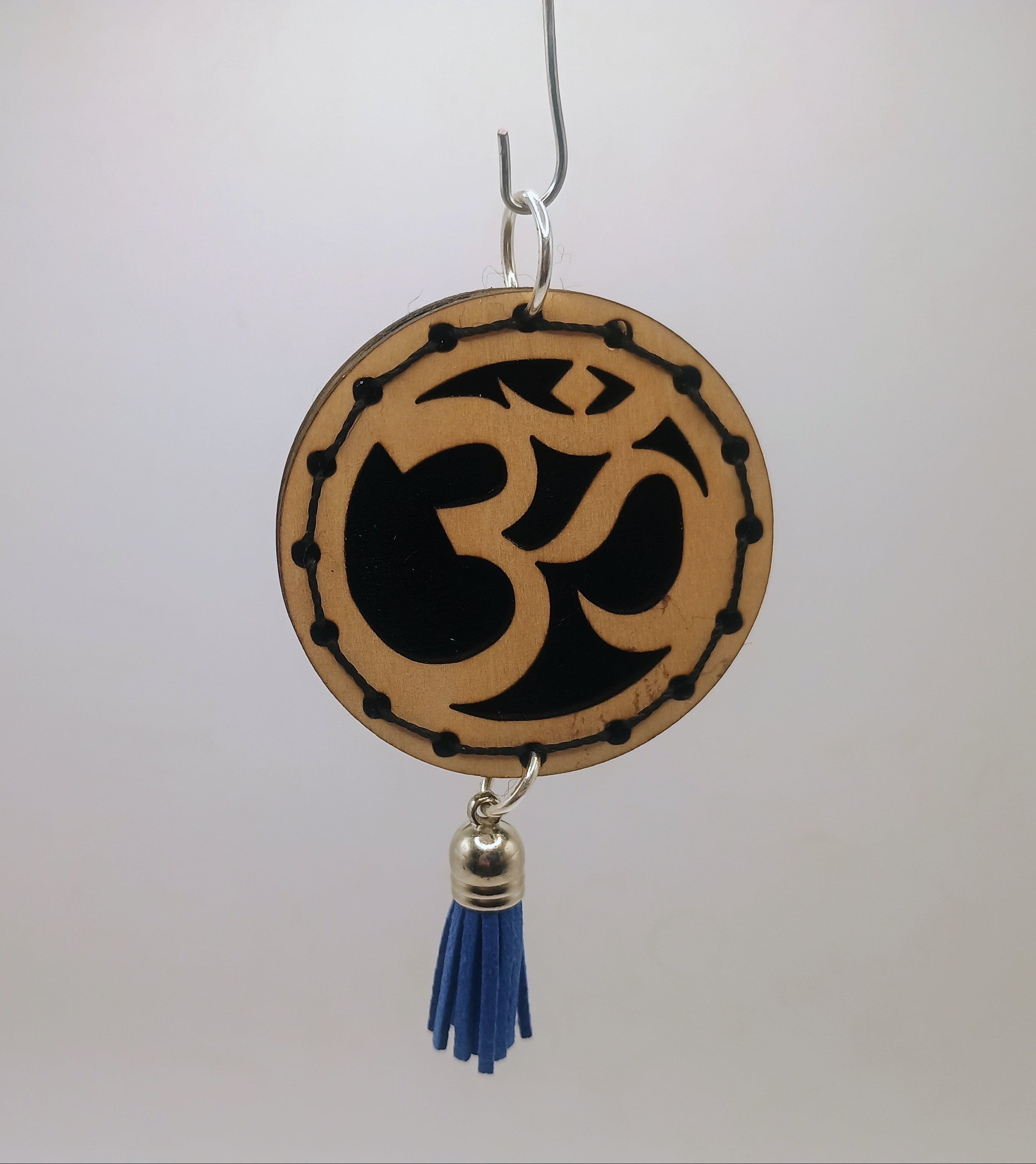 Decorative hanging item with Om symbol and blue tassel on a plain background