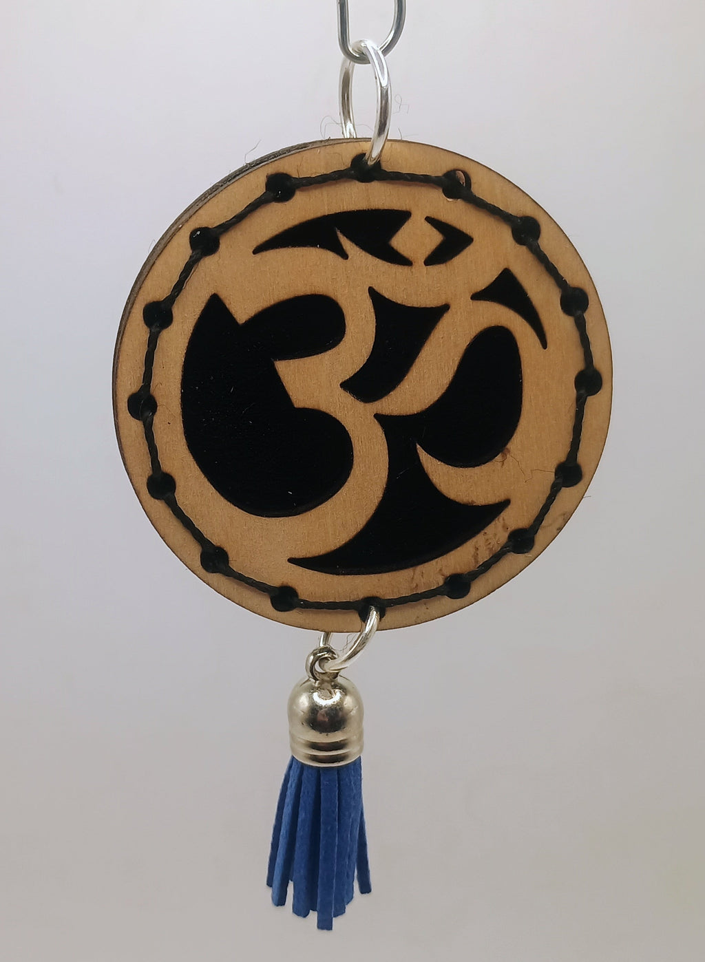 Decorative hanging item with Om symbol and blue tassel on a plain background