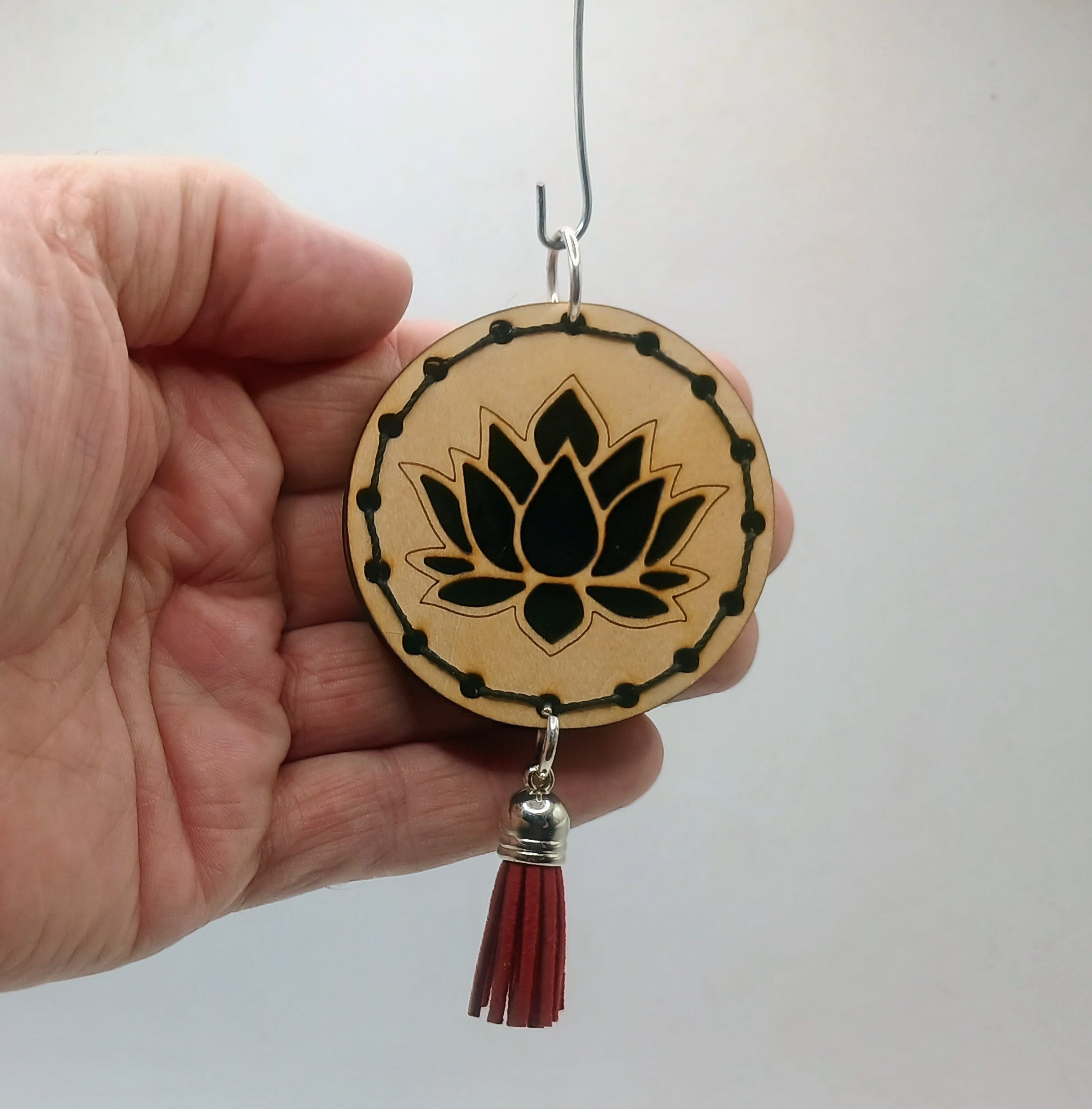 Hand holding a wooden pendant with a lotus design and red tassel against a white background