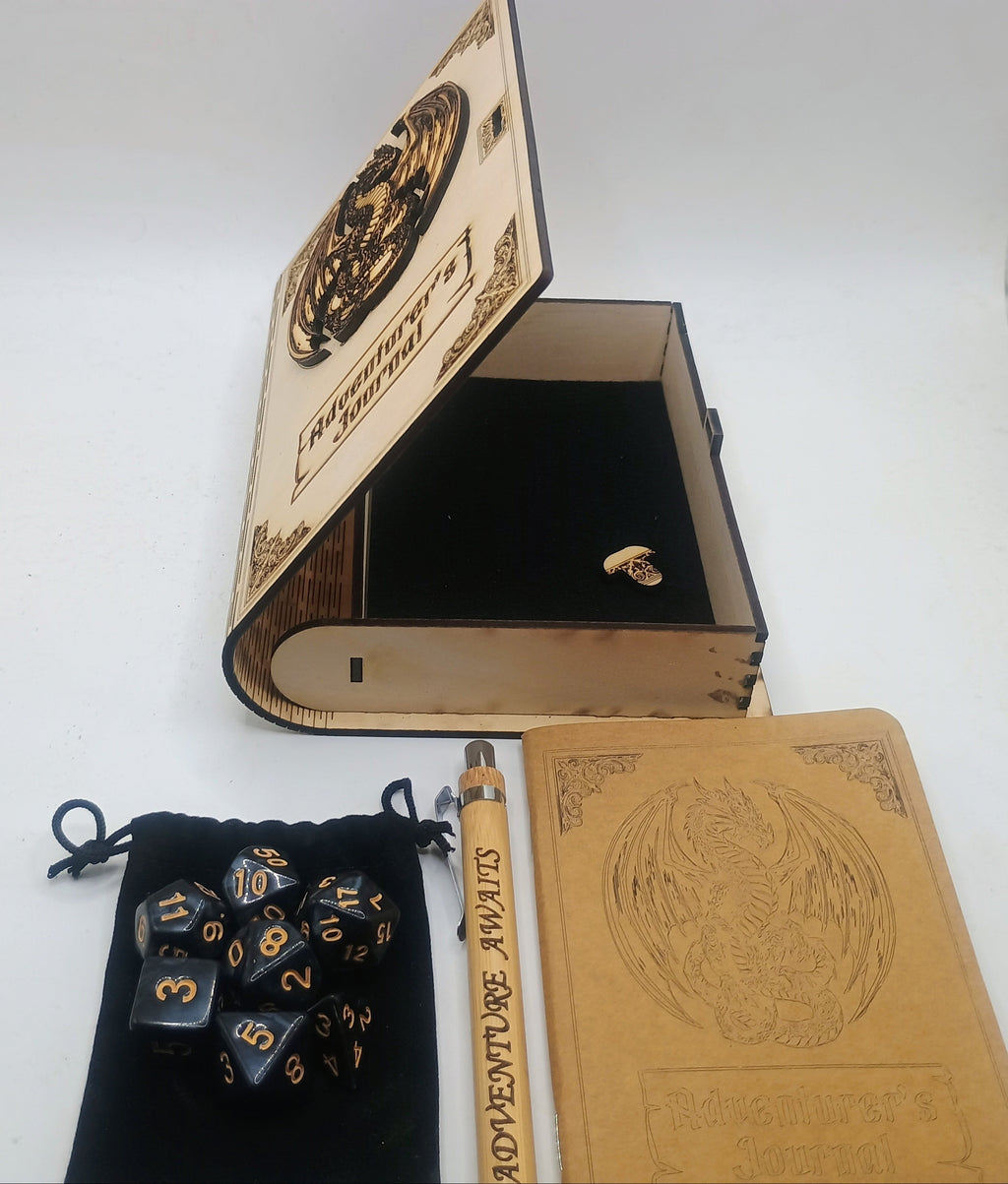 A themed tabletop gaming set featuring a miniature book-shaped box with an engraved cover, a black velvet pouch containing polyhedral dice, a tan notebook, and a wooden pen