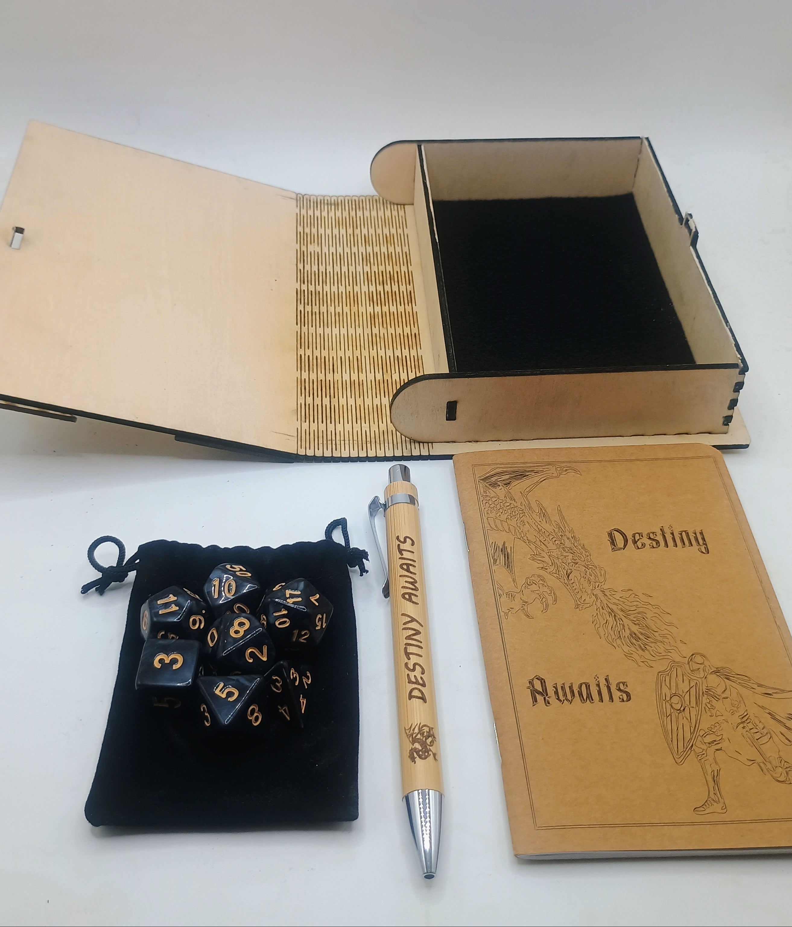 A tabletop product set including a wooden keepsake box with black interior, a pen and journal engraved with 'Destiny Awaits,' and a set of polyhedral dice with a small black pouch.