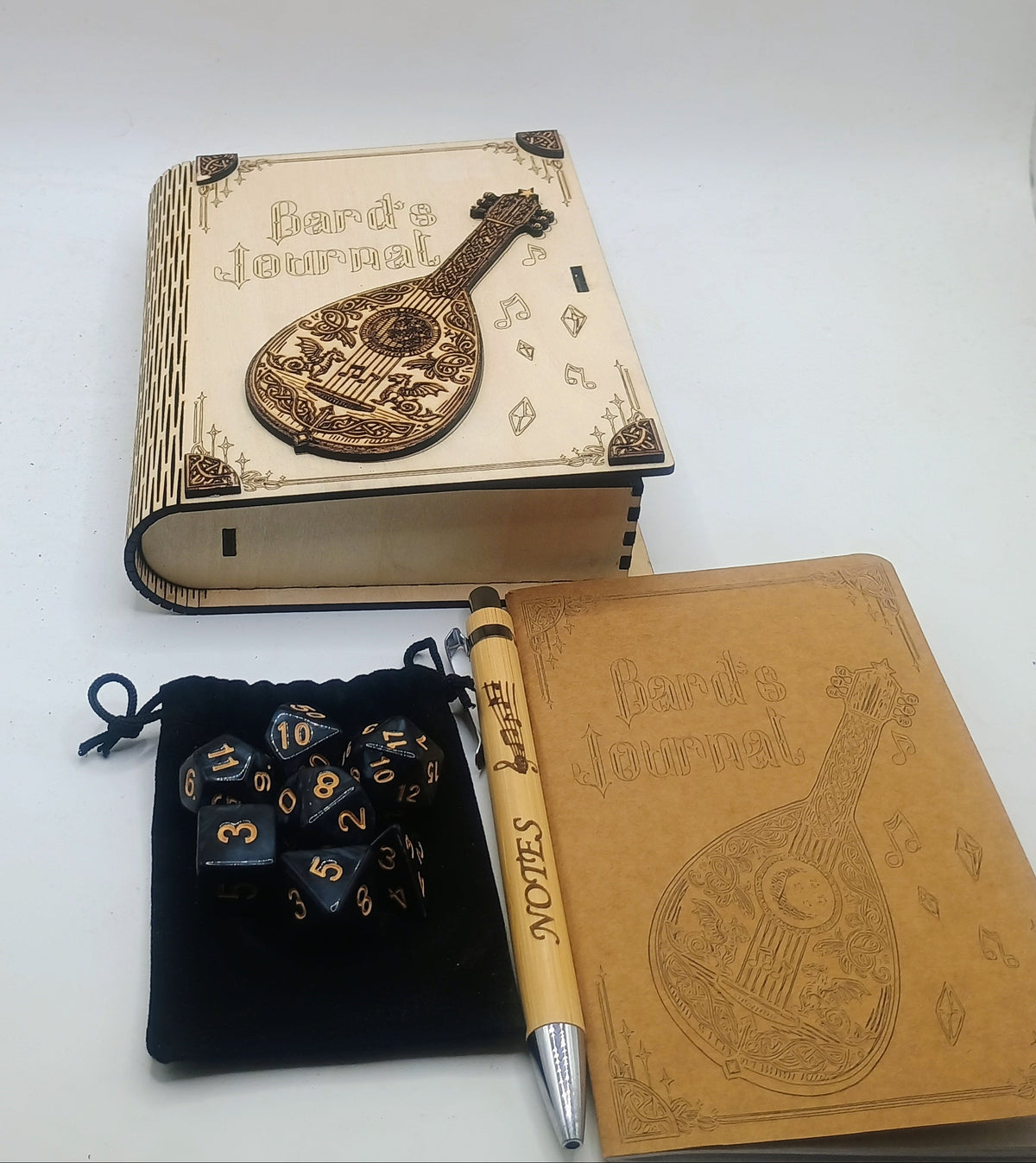 A tabletop product display featuring a decorative journal with a guitar illustration, a matching pen, a small black pouch, and polyhedral dice.